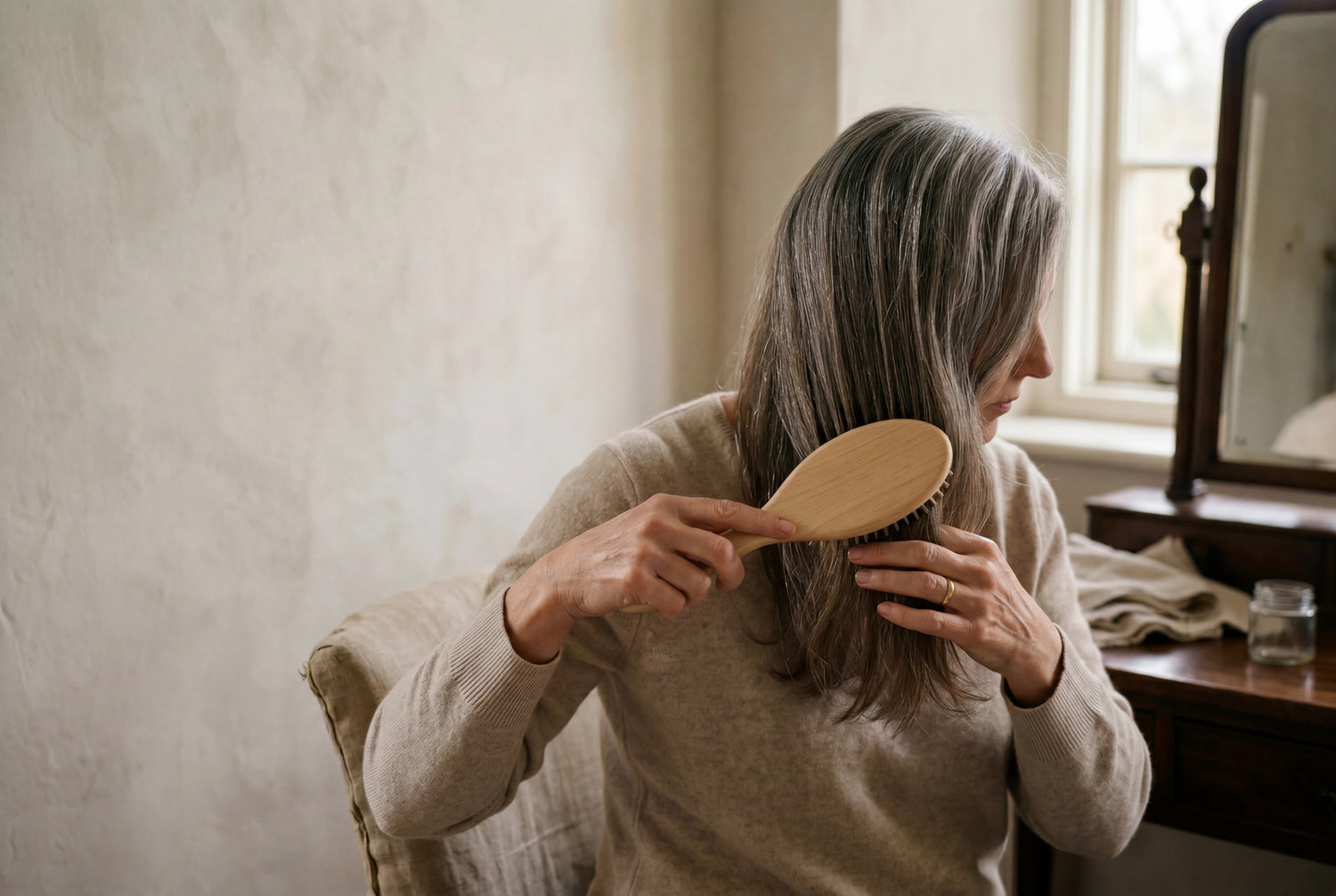 Woman gently brushing raw virgin salt-and-pepper hair extensions in soft warm window light