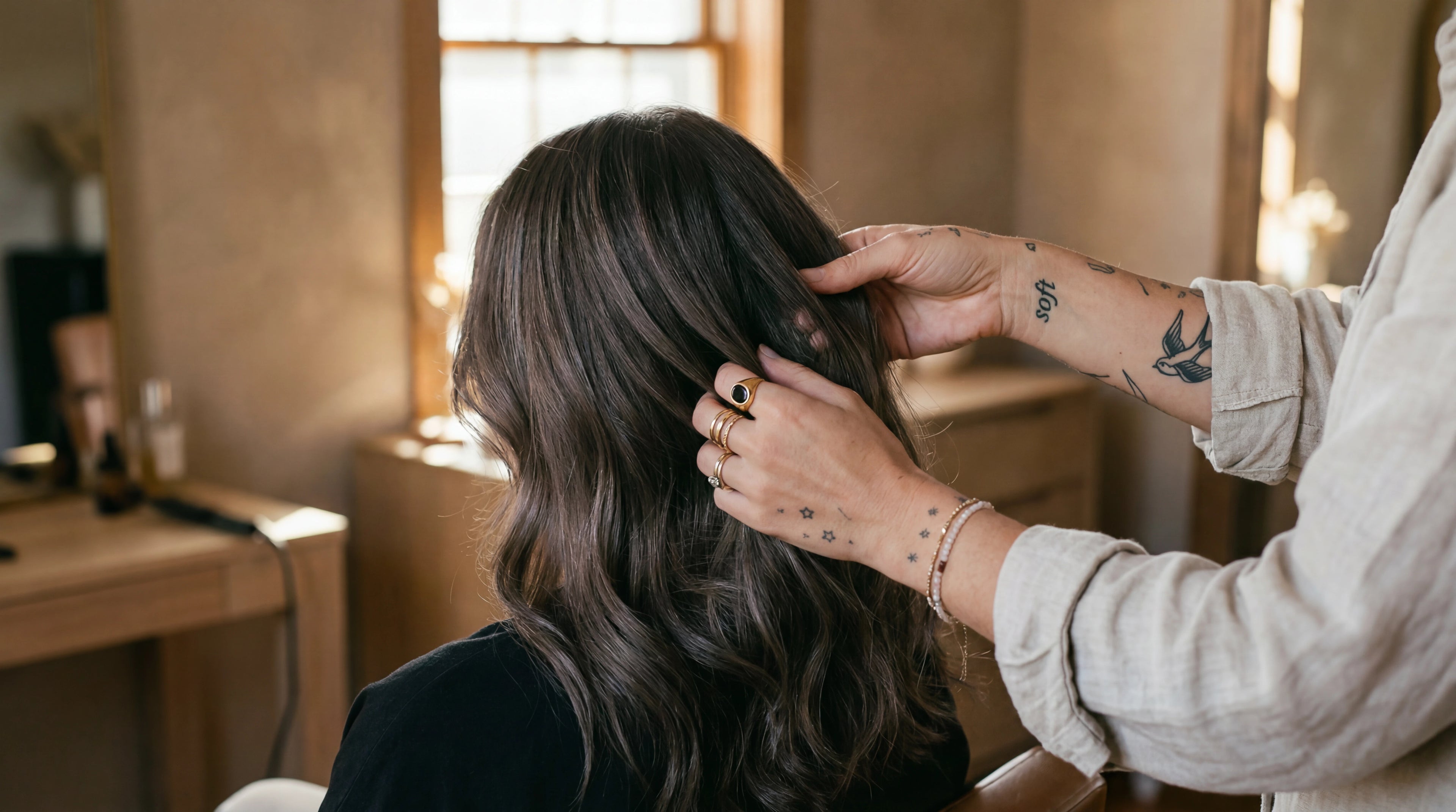 Salon stylist working with L'hair raw virgin hair extensions in a warm atelier setting from behind