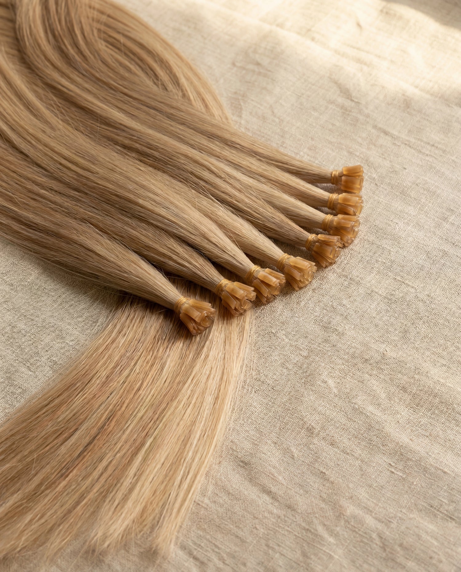 Close detail of L'hair keratin-tip hair extension bonds in warm honey blonde, the protein-bond construction