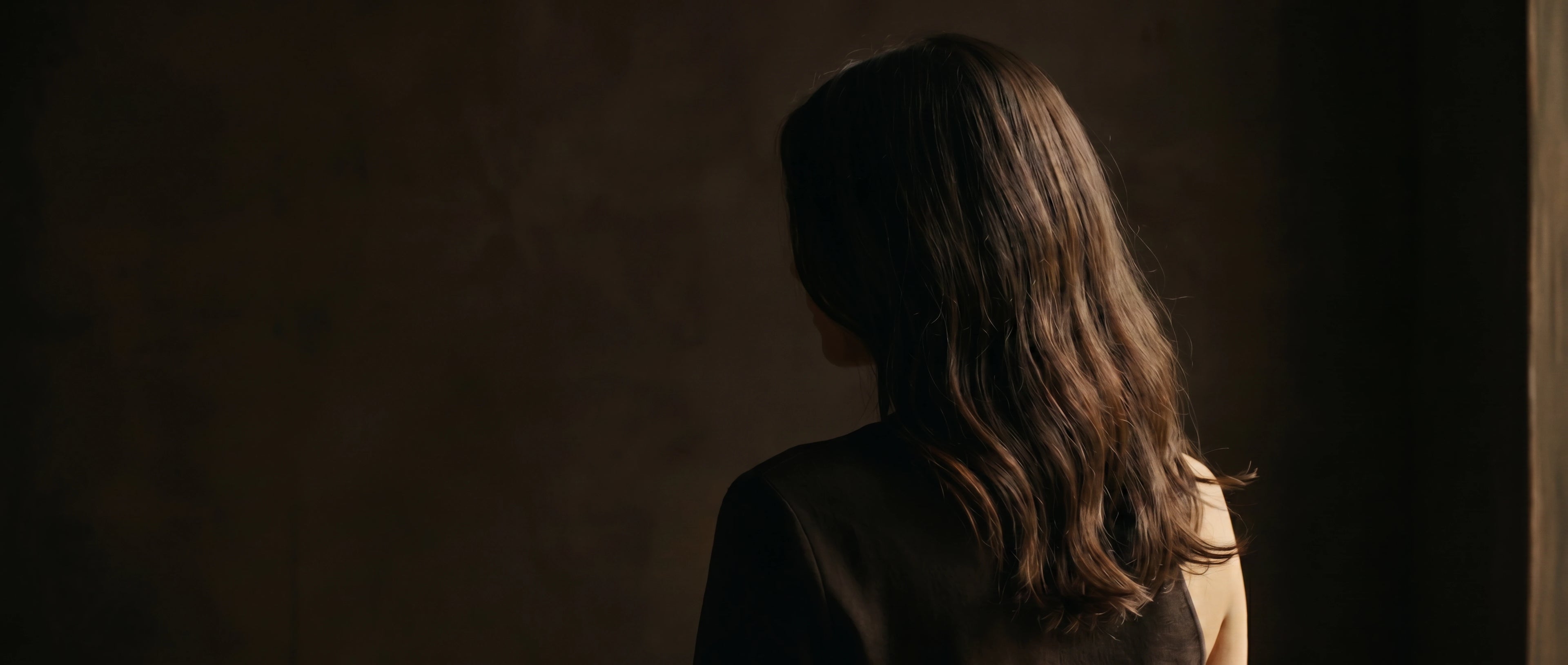 Editorial portrait of woman with long brunette L'hair extensions in soft low-light warm interior