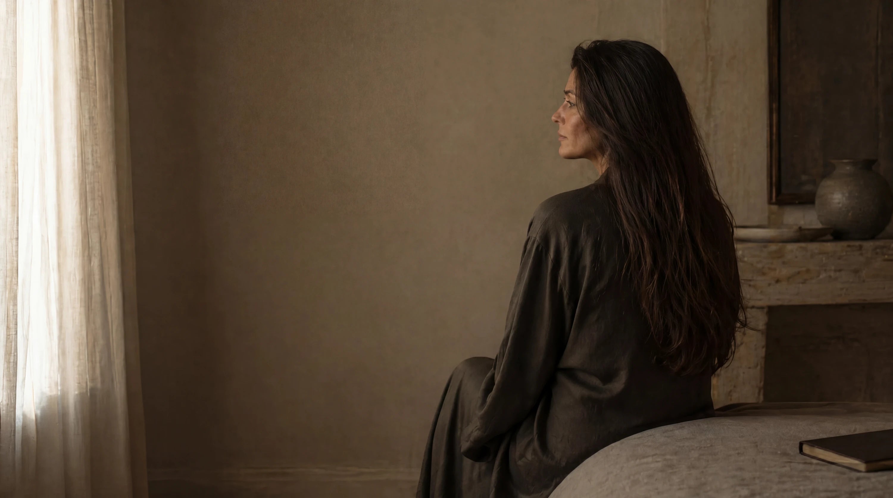 Woman with long raw virgin brunette hair extensions photographed from behind in warm natural window light